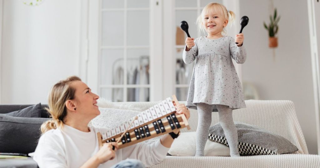 Nasmijane djevojčica sa zvečkama i majka s udaraljkama
